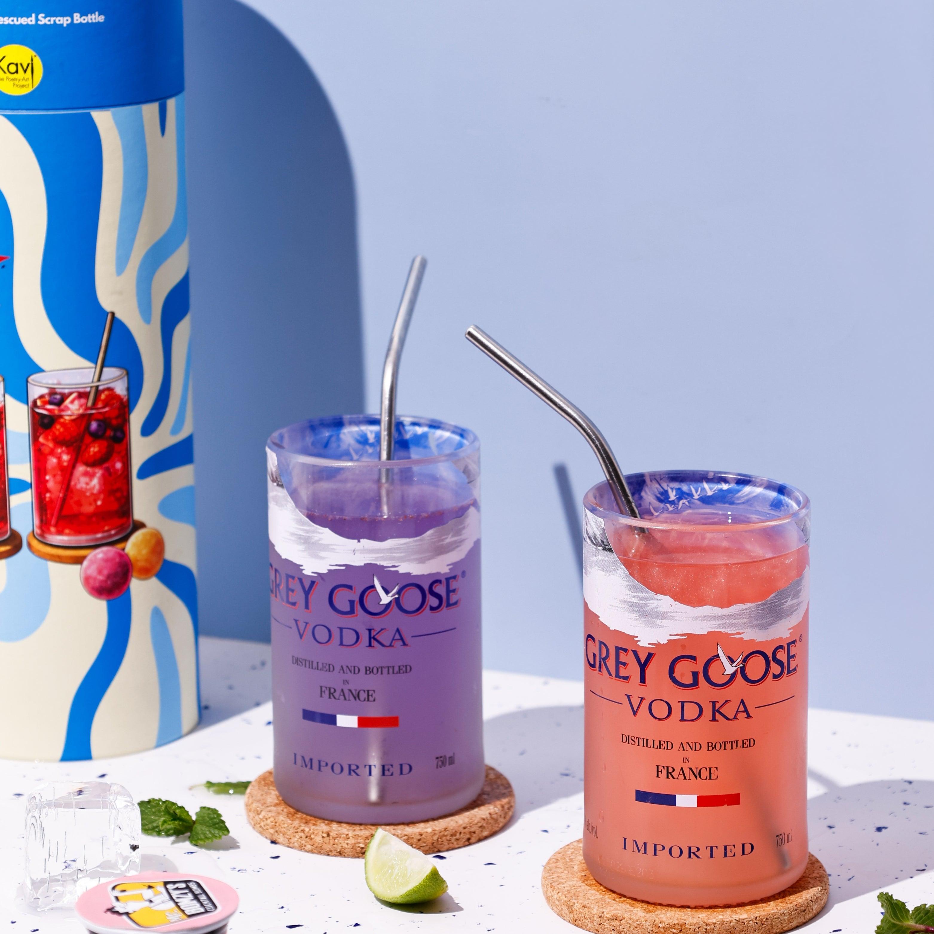 Two Grey Goose vodka cocktails with straws on a white surface with a blue background