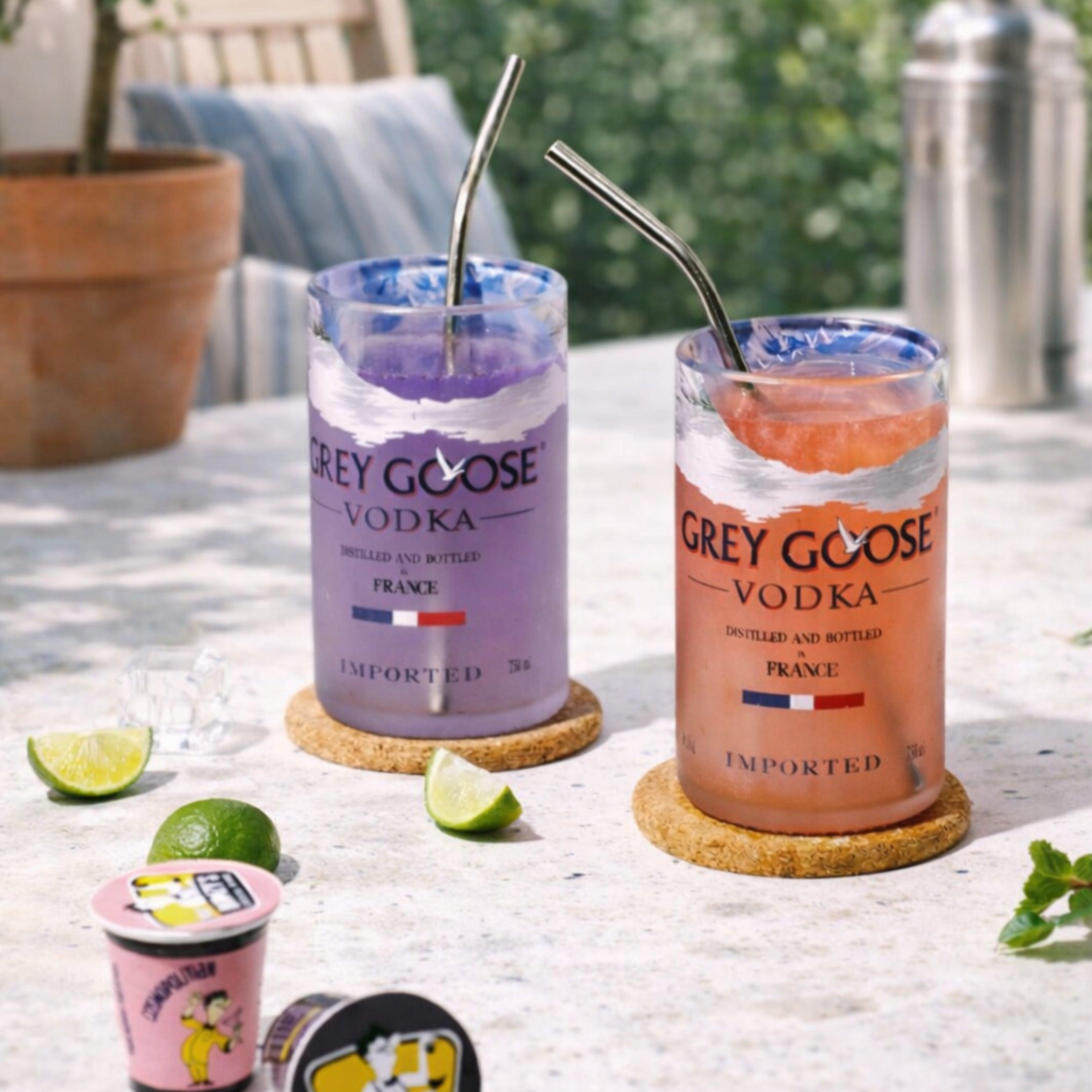 Two Grey Goose vodka cocktails with straws on a table outdoors.